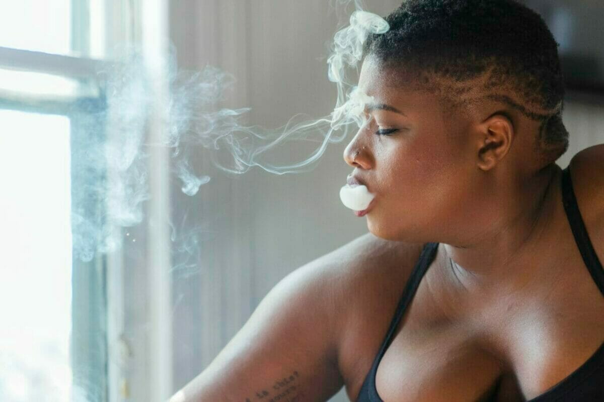 Jessamyn Stanley blowing smoke out of her mouth in profile shot in black strappy top