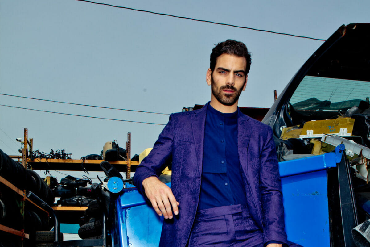 Nyle DiMarco in purple suit looking at camera in front of trash bin
